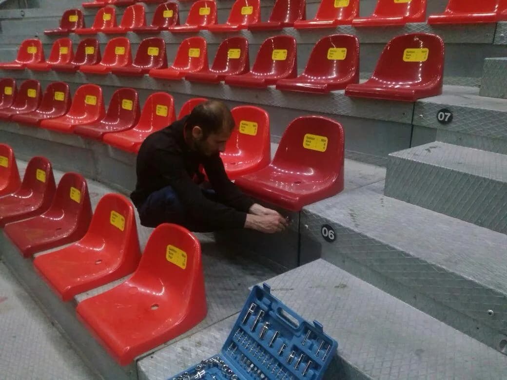 Worker fastening a red molded spectator seat to a temporary grandstand